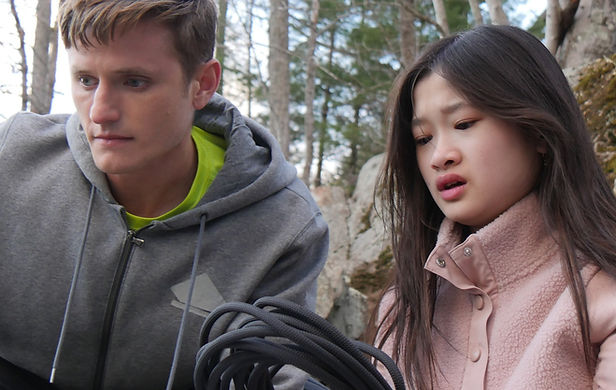 A young man and woman pause together in the forest holding climbing rope