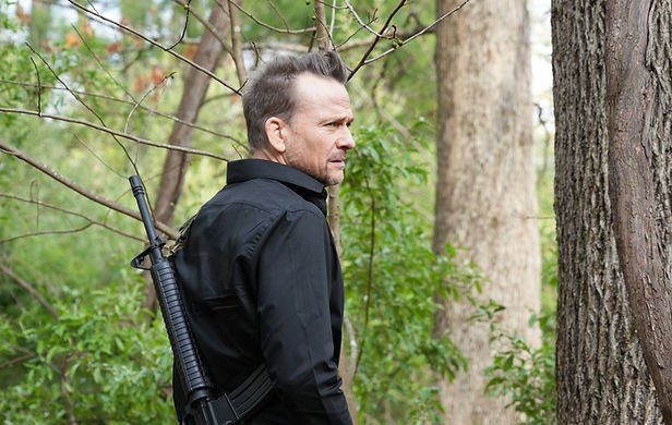 A figure in black carrying a rifle among the trees